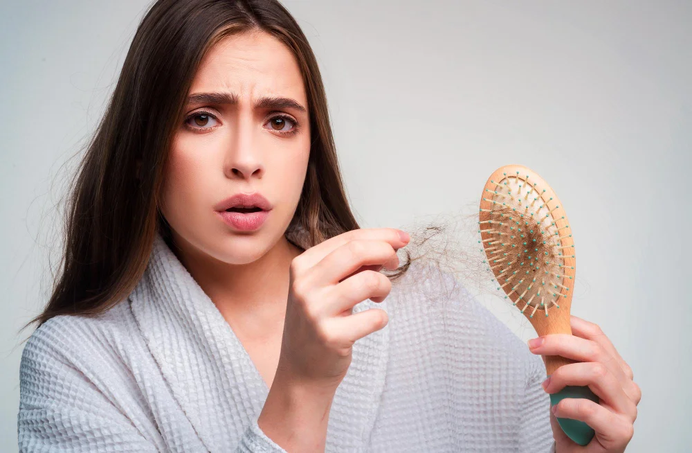 Concerned woman holding hairbrush with excessive amount of hair loss visible on the brush