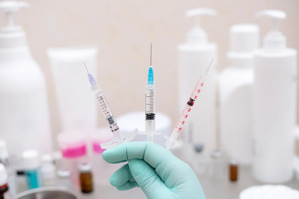 Medical professional holding three glutathione injection syringes in sterile gloved hand at dermatology clinic for skin whitening treatment
